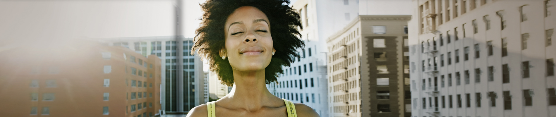 Woman smiling with eyes closed, city view behind her